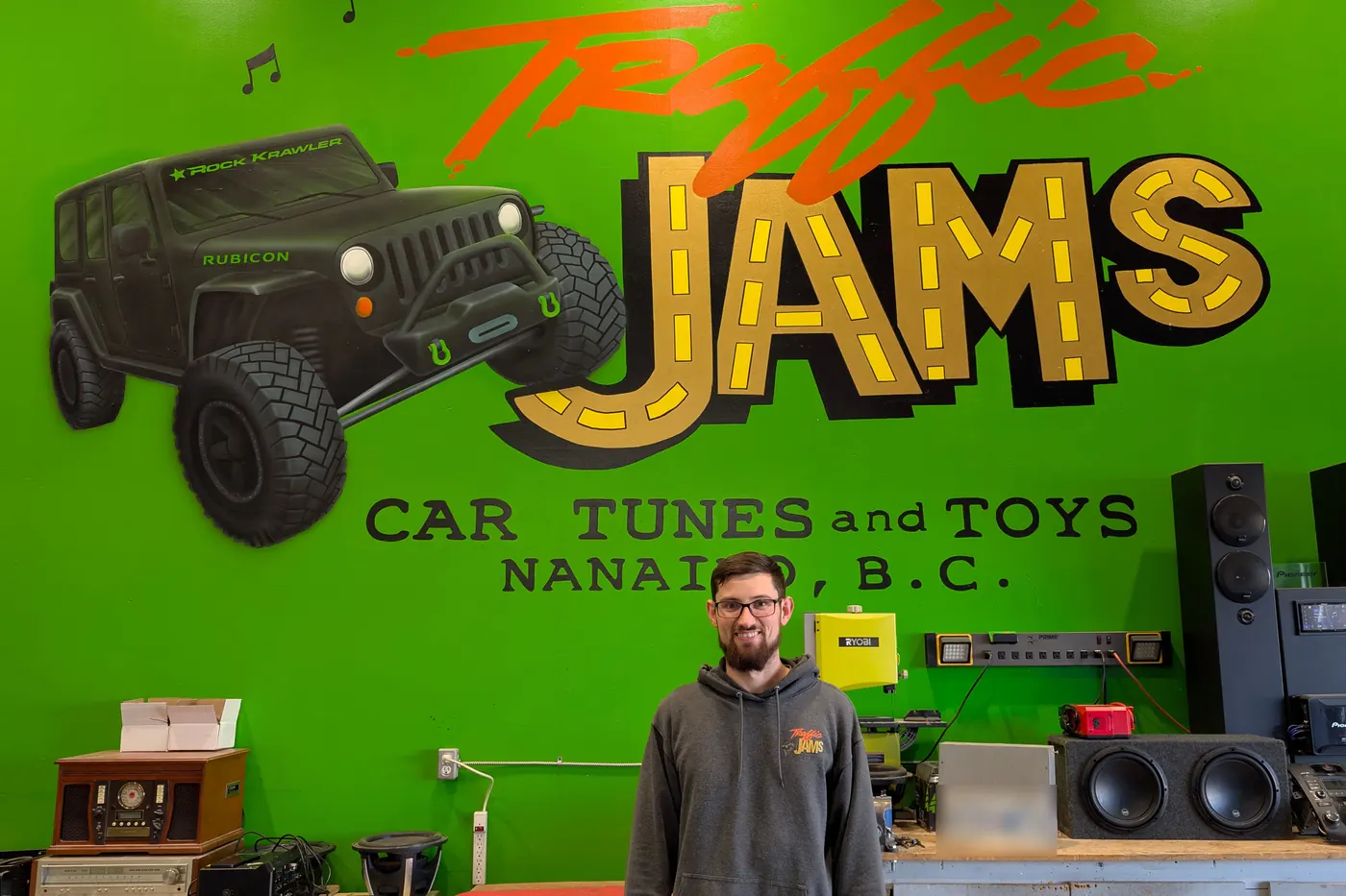 Josh Belanger standing under the hand-painted Traffic Jams Car Tunes and Toys mural in his Nanaimo shop