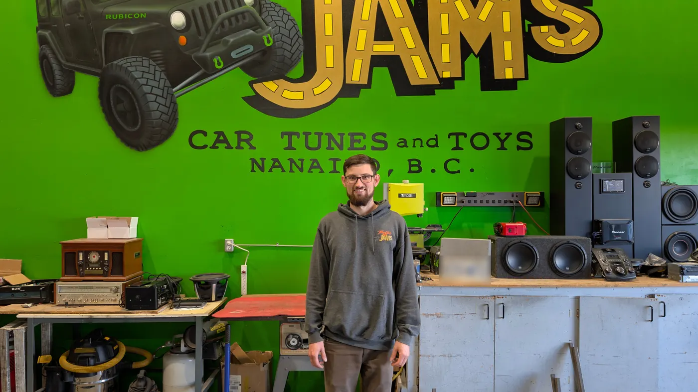 Josh in front of the shop mural and his wall of speakers and subwoofers